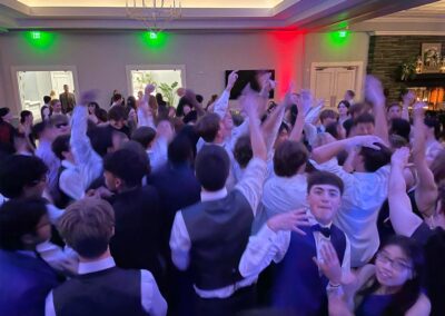 Large group of students dancing and throwing their hands in the air at high school prom