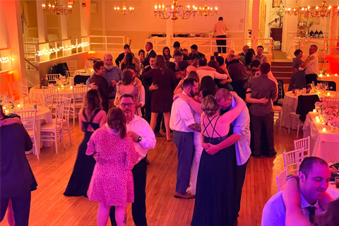 Image of large group of people slow dancing at wedding with radiating orange lights